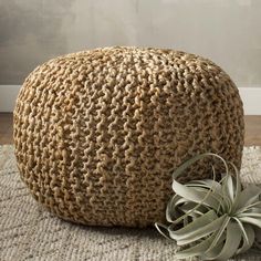 a plant sits on the floor next to a large knitted round ottoman with an air plant in it