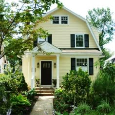 a yellow house with black shutters and white trim on the front door is surrounded by greenery