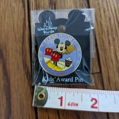 mickey mouse pin sitting on top of a wooden table next to a measuring tape and ruler