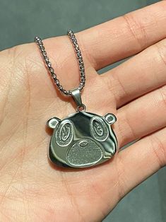 a hand holding a small silver pendant with an animal face on it's side