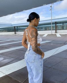 a woman with tattoos on her back standing in front of an empty parking lot at an airport