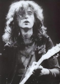 a black and white photo of a man with long hair holding a guitar in his right hand