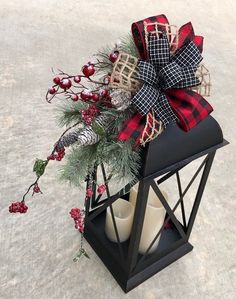 a candle holder decorated with red and black plaid ribbon, pine cones, berries, and holly