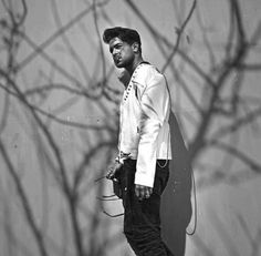 a man standing in front of a wall with his hands in his pockets and looking at the camera