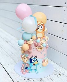 a cake decorated with balloons and other decorations on a white wooden table next to a wall