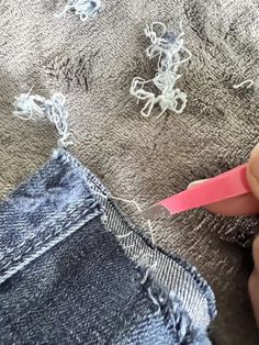 someone is cutting through the holes in their jean pants with a pink handled scissors and thread