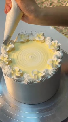 a person is decorating a cake with white icing on a silver platter