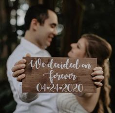 a man and woman holding up a wooden sign