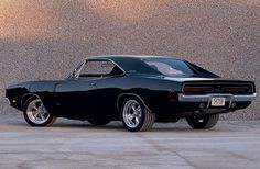 a black muscle car parked in front of a wall