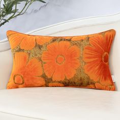 an orange floral pillow sitting on top of a white couch next to a potted plant