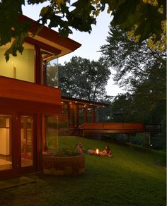 two people sitting around a fire pit in front of a modern home at night time