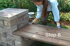 a woman bending over to put something in a bucket on top of a wooden bench