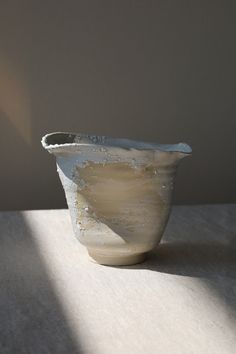 a white vase sitting on top of a table next to a shadow from the wall