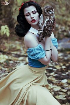 a woman dressed as snow white holding an owl in her right hand while sitting on the ground