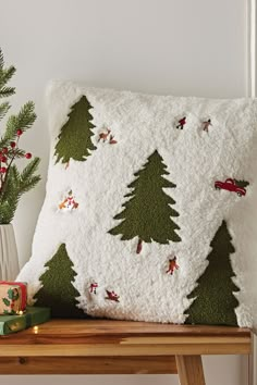 a white pillow with christmas trees on it next to a potted plant and small presents