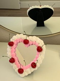 a cake shaped like a heart with cherries on it and a mirror in the background