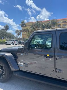 a gray jeep parked in front of a building with palm trees on the other side