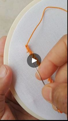 someone is stitching an orange thread on a white piece of fabric with their fingers