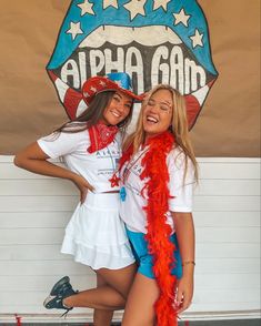 two young women posing for a photo in front of an american game sign with red, white and blue feathers