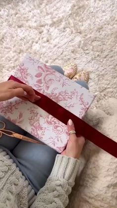 a woman is sitting on the floor holding up a gift box with a red bow