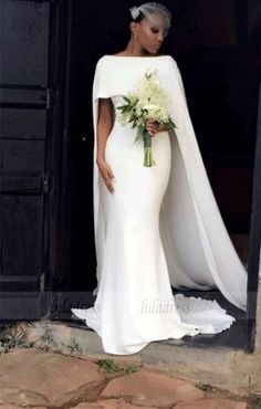 a woman in a white gown with a cape on her head and flowers in her hand