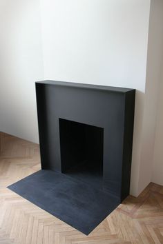 an empty black fireplace in a room with parquet floor and white wall behind it