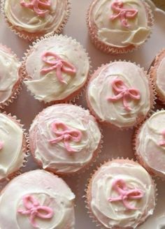 cupcakes with white frosting and pink bows are arranged on a platter