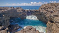 a man standing on the edge of a rocky cliff over looking the ocean and rocks