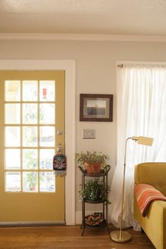 a living room with a yellow door and white curtains