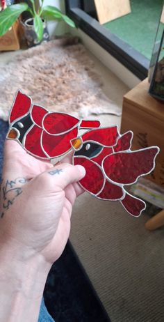 a person holding up a stained glass cardinal bird in front of a window with a plant behind it