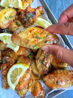 someone is pointing at some chicken wings with lemons and parsley