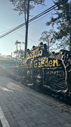 a sign that reads baguio botanical garden on the side of a road in front of some trees