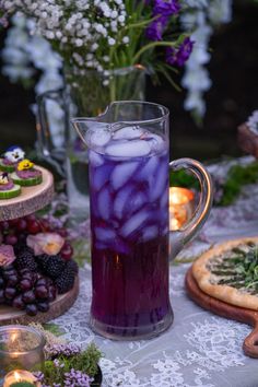 a pitcher filled with liquid sitting on top of a table next to pizzas and flowers