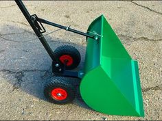 a green wheelbarrow sitting on the ground next to it's red wheels