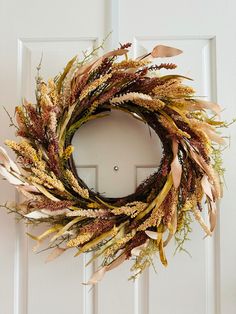 a wreath is hanging on the front door with dried grass and leaves around it's edges