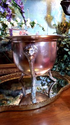 an ornate metal bowl with a snake handle on a wooden table in front of flowers