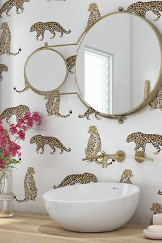 a white sink sitting under a mirror next to a wall with leopards on it