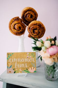 cinnamon buns on a table with flowers and a sign