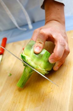 a person cutting up an artichoke on top of a wooden board with a knife