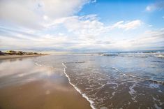 the beach has waves coming in to shore and blue sky with white clouds above it