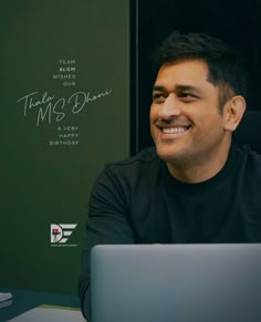 a man sitting in front of a laptop computer smiling at the camera while wearing a black shirt