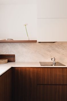 a modern kitchen with wooden cabinets and white counter tops, including a single flower in a vase