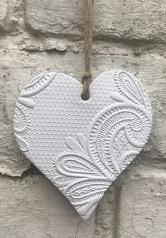 a white heart hanging from a rope on a brick wall with an intricate design in the middle