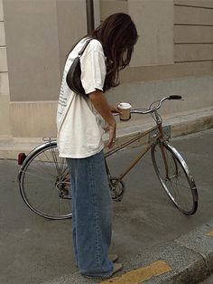 a person standing next to a bike with a cup of coffee on it's handlebars