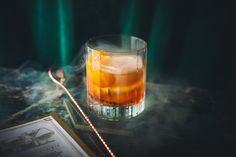 a glass filled with liquid sitting on top of a table next to an open book