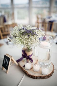 a vase filled with white flowers sitting on top of a wooden slice next to candles