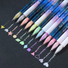 several different colored pens are lined up on a black surface with stars and hearts drawn on them