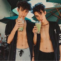 two young men drinking green smoothies under an umbrella