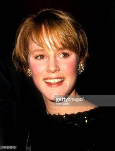 a woman in black dress smiling at the camera with her hand on her hip and wearing earrings