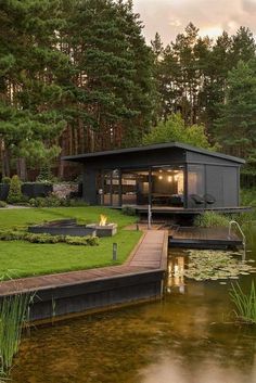 a small house sitting on top of a lush green field next to a lake and forest